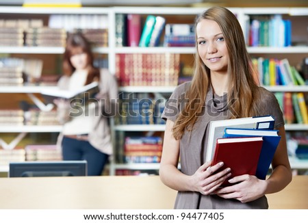 Studying young teenage college student girl  in a library with books in front of book shelves