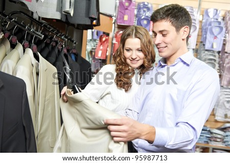 Young man and woman choosing suit jacket during apparel shopping at clothing store