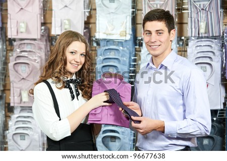 Young man choosing shirt and necktie during apparel shopping at clothing store
