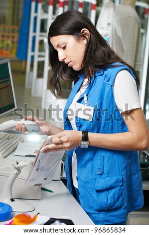 Young shop assistant selling clothing in shop at cash desk