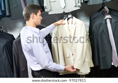 Young man choosing suit jacket during apparel shopping at clothing store