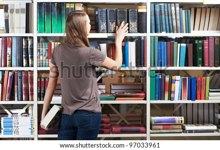 young college student in a library selecting books from bookshelf during self education