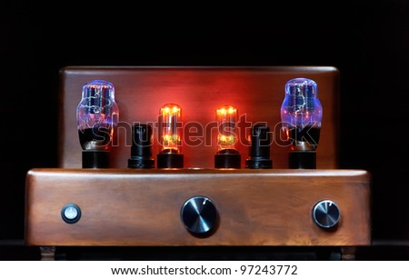 Old-fashioned electronic device amplifier with glowing bulb diode lamp for sound reproduction over dark background