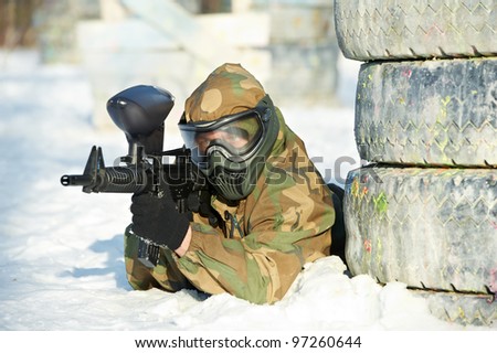 paintball extreme sport player wearing protective mask and comouflage clothing with marker gun at winter outdoors