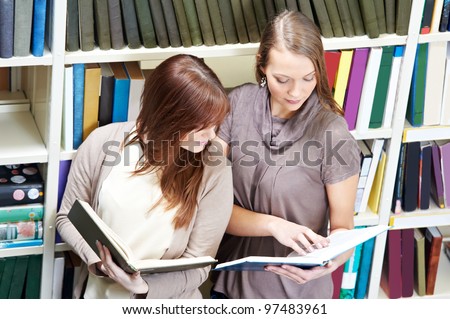Studying young teenage college student girl  in a library with books in front of book shelves