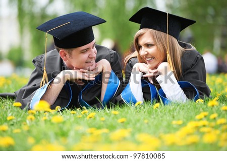 two graduate students guy and girl lying on spring grass smiling