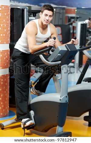 smiling fitness man at legs muscles exercises with bicycle training machine station in gym