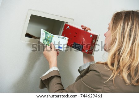Money safety and security. Woman put savings cash into wall safe