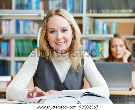 Young pretty smiling woman in a library with books at self-education
