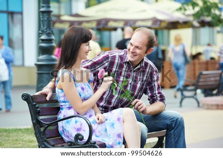 Man presenting flower to girl at street bench cafe on a date outdoors
