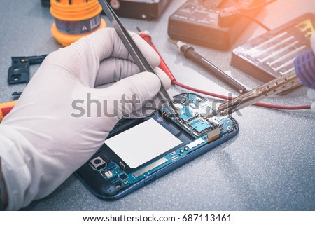 The asian technician repairing the smartphone's motherboard by soldering in the lab. the concept of computer hardware, mobile phone, electronic, repairing, upgrade and technology.