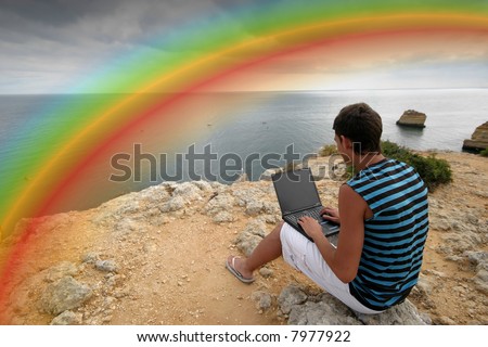 boy working on portable pc under a raibow