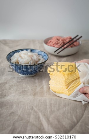 Female hands holding a stack of wonton wrappers.  Raw shrimp and raw ground pork in the background.
