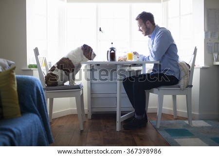 Young man eating breakfast with dog