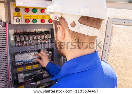 The electrician adjusts the electrical cabinet. engineer in helmet is testing electrical equipment. Maintenance of electric system. Worker diagnostic of automation panel