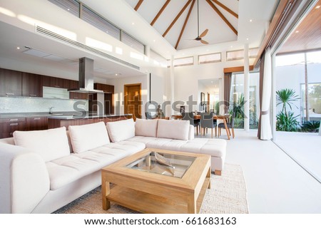Luxury interior design in living room of pool villas. Airy and bright space with high raised ceiling, sofa, middle table, dining table and open kitchen