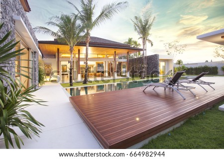 Exterior design of spacious modern luxury pool villa. Feature wooden decking, sunbed, big swimming pool and greenery garden