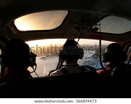 Inside helicopter, pilot and 2 passengers taken from the rear seat of helicopter with the view overlooking a lake in Sweden