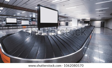 Wide-angle view of an empty luggage conveyor belt with the rubber sections and blank white LCD informational screen mockup on the top and behind; bright arrival zone of a contemporary airport terminal