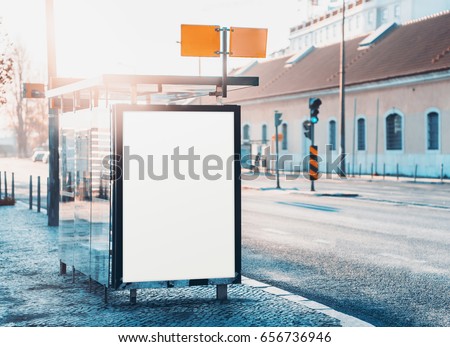 Glass city bus stop with mock-up of information poster, vertical blank billboard near road, empty white placeholder frame in urban settings with copy space for logo or advertising text on sunny day