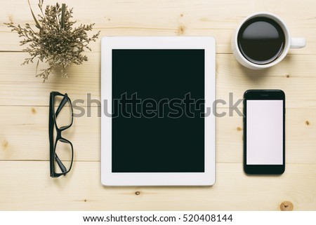 Top view of white tablet blank black screen for advertisement display or other app design with smartphone, coffee cup and eyeglasses on wood background
