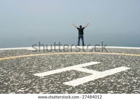 young man with arms open contemplating the ocean in foggy day in the heliport