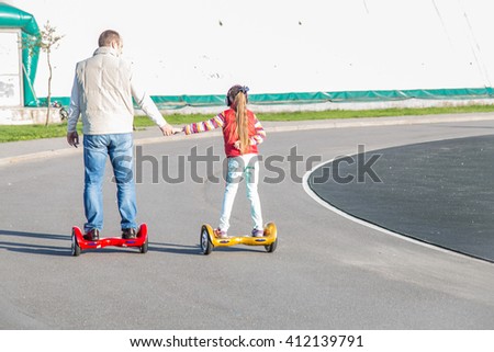 Father and daughter on shoulders riding on modern red and yellow electric mini hover board scooters