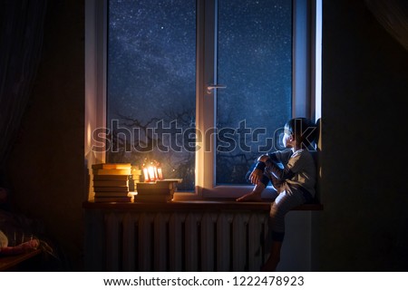 The child sits on the windowsill at night looking at the stars and dreams.