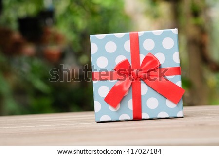 light blue and white polka dot with red ribbon gift box on the wood table green selective blue focus background