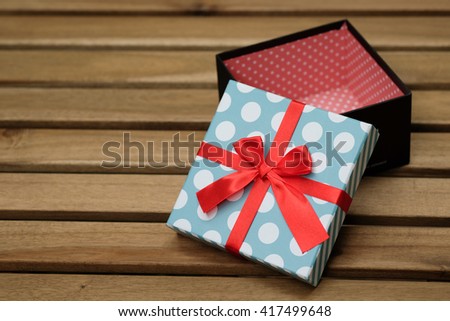 light blue and white polka dot with red ribbon gift box on wood table with green background