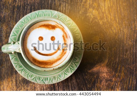 Smile of latte coffee with sunshine on wooden background.(Top view)