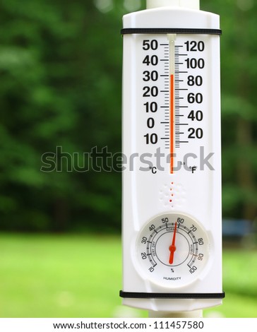 An new outdoor mercury thermometer and humidity gauge on a pole reading the outdoor summer temperature and humidity using a shallow depth of field and selective focus with room for your text.