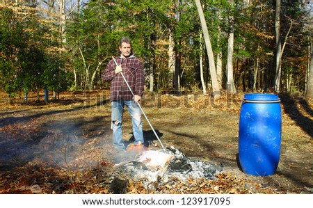 A man working a burning pile of trash and debris along side the edge of the woods