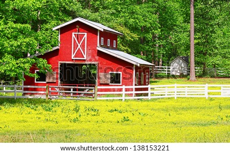An unusual two story old red horse barn outside among the woods in a buttercup field