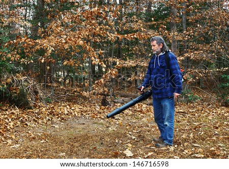 A middle aged long gray haired white male outside working on a fall day blowing leaves out in the yard