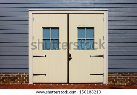 Some old side by side wooden doors with window frames in them on the side of a building with a brick foundation and brick entrance way to them