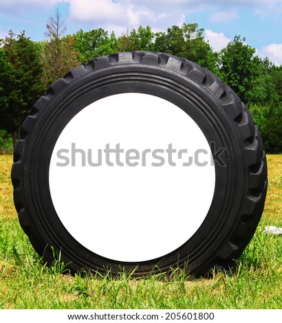 A large heavy equipment tire in a field along the woods on a summer day with a large round white cardboard center with room for any type of text or design to fill your needs