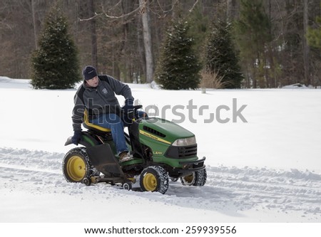 GLOUCESTER, VA - FEBRUARY 17 2015: An unknown man uses his John Deere lawnmower deck to clear snow, Deere & Company an American corporation manufactures agricultural, construction & forestry machinery