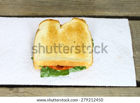 A fresh made bacon lettuce and tomato sandwich served on a paper towel on top of an old wooden picnic table outside during the summer