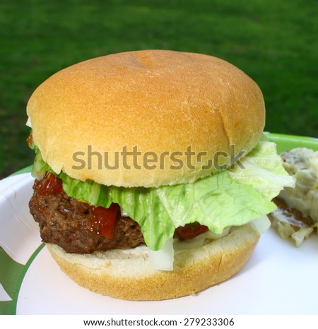 A fresh made hamburger on a paper plate on an old  wooden picnic table outside during the summer