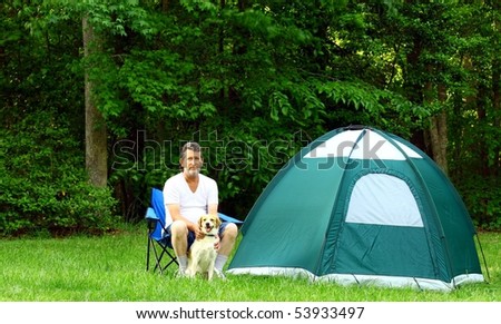 A man and his dog sitting outside in the woods next to their tent