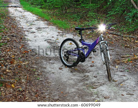 A mountain bicycle with a flashlight mounted on the handle bars on a trail through the woods
