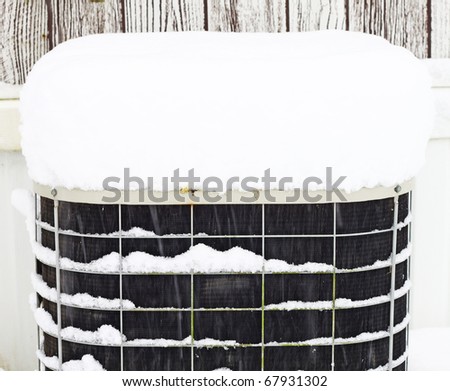 A frozen snow covered AC unit outside while it is snowing on a winter day with room for your text.