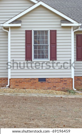 A window in a vinyl sided house with a curtain in it on a brick foundation along with gutters on both sides with room for your text.