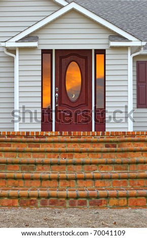 A staircase leading to a patio and a back door entrance with a sunset reflecting in the glass of a ranch house with room for your text.