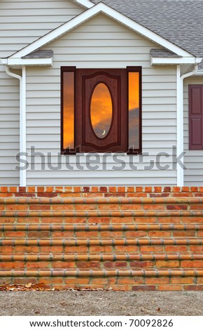 A Beautiful wood framed window with a sunset reflection in it in a vinyl sided house with a brick staircase leading up to the back patio along with gutters on both sides with room for your text.