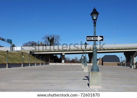 A Lamp lined concrete parking lot at the foot of a bridge in Yorktown Virginia and a one way sign going in the direction of travel for the bridge traffic with room for your text.