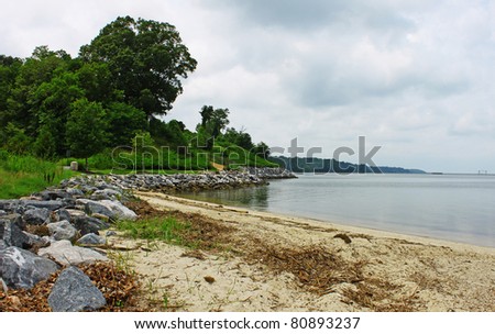 A sandy rock lined Beach of the York river in Yorktown Virgina on an overcast summer day looking up river to the Naval Weapons Station with room for your text.
