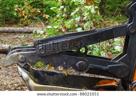 An Excavator bucket with the jaw attachment on it used for lifting trees and debris resting on the ground outside in the woods with room for your text.