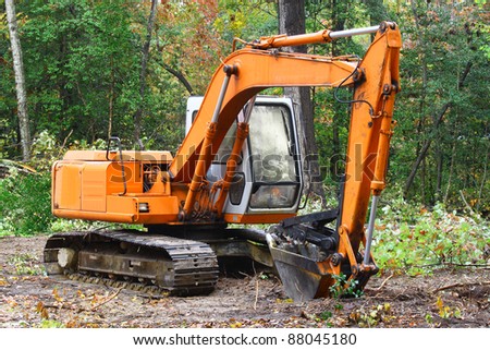 A construction Excavator used for excavating of trees debris and anything else needed resting on the ground outside in the woods with room for your text.